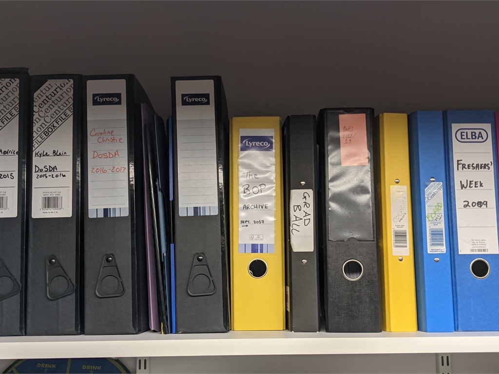A line of colourful box files on a shelf.
