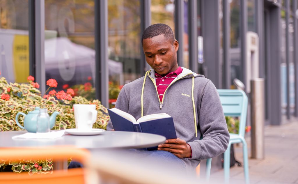 A student sits outside Rector's Café reading a book.