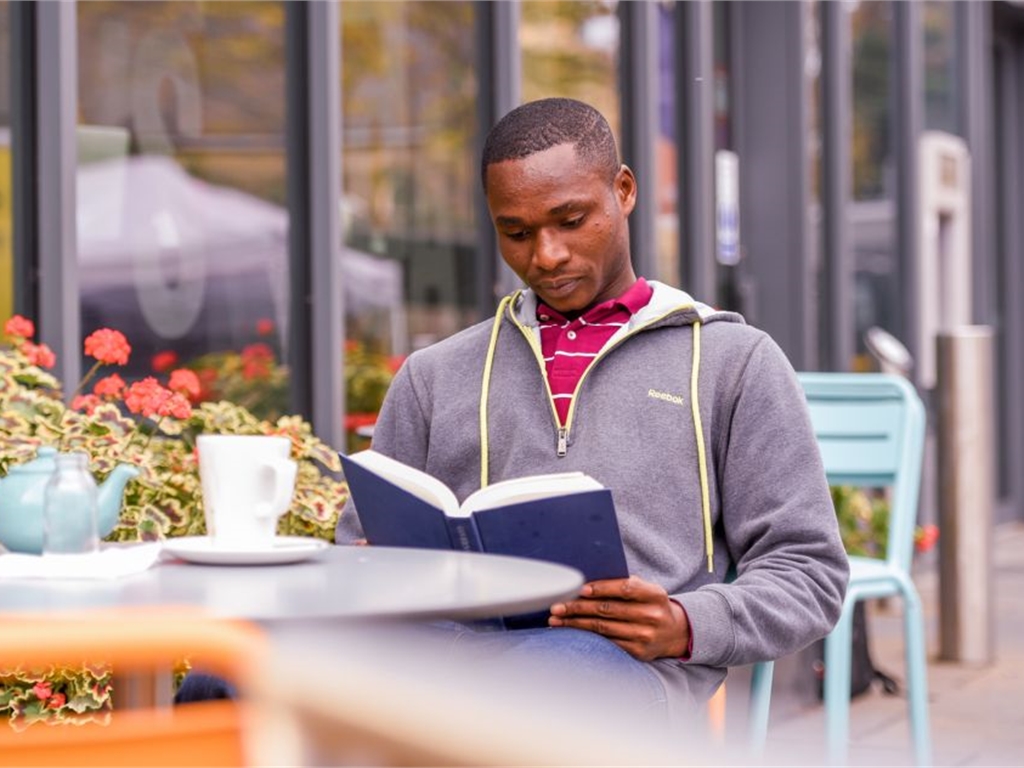 A student sits outside Rector's Café reading a book.