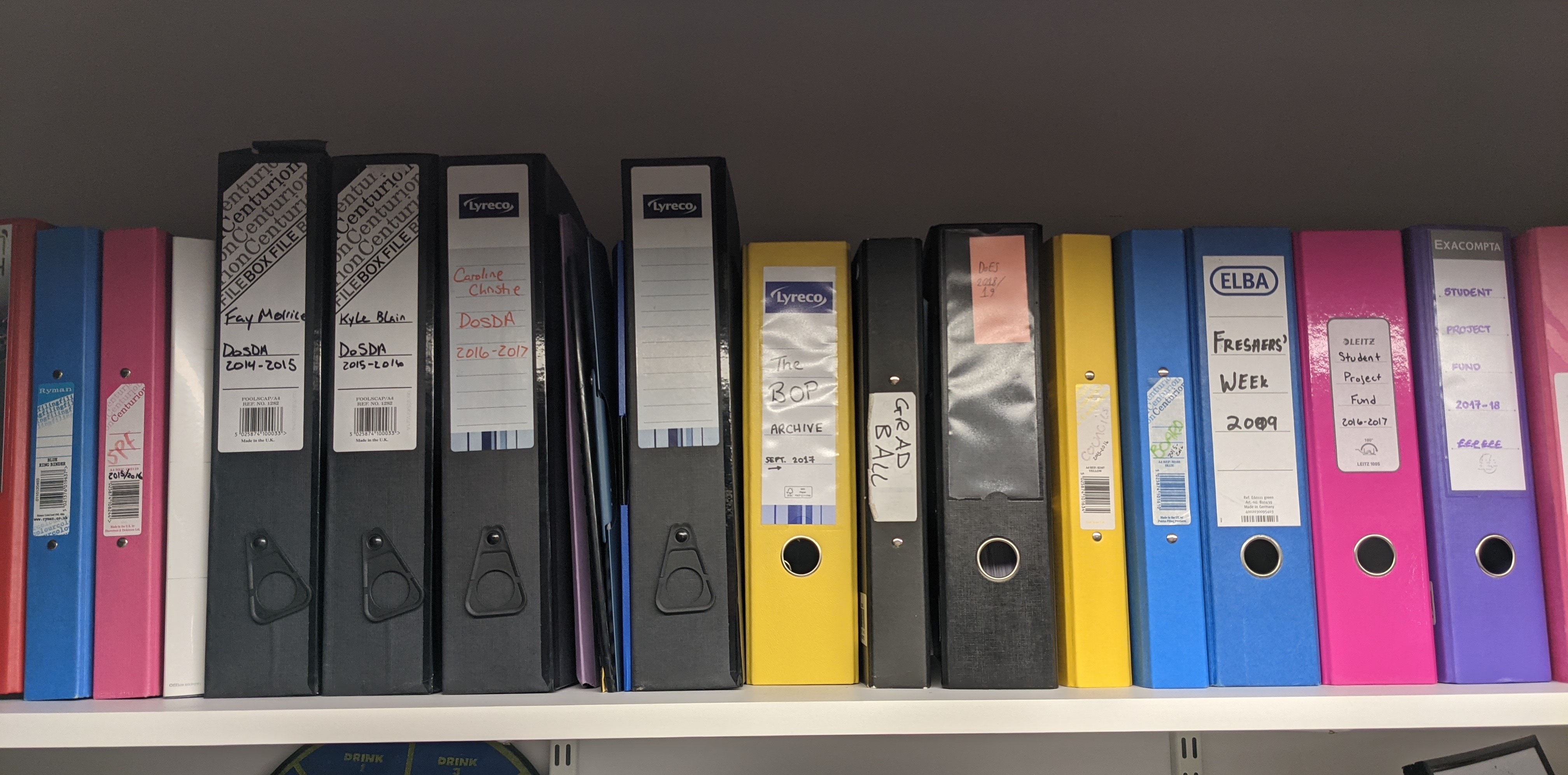 A line of colourful box files on a shelf.