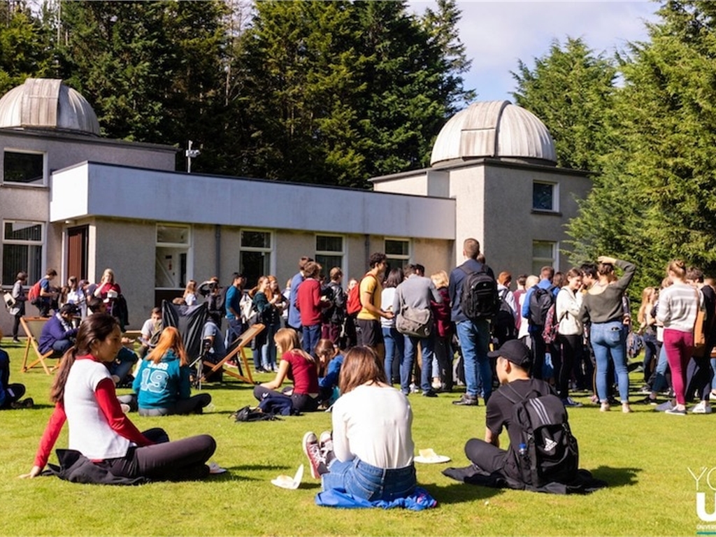 People outside the observatory, they are sitting on the grass and chatting.