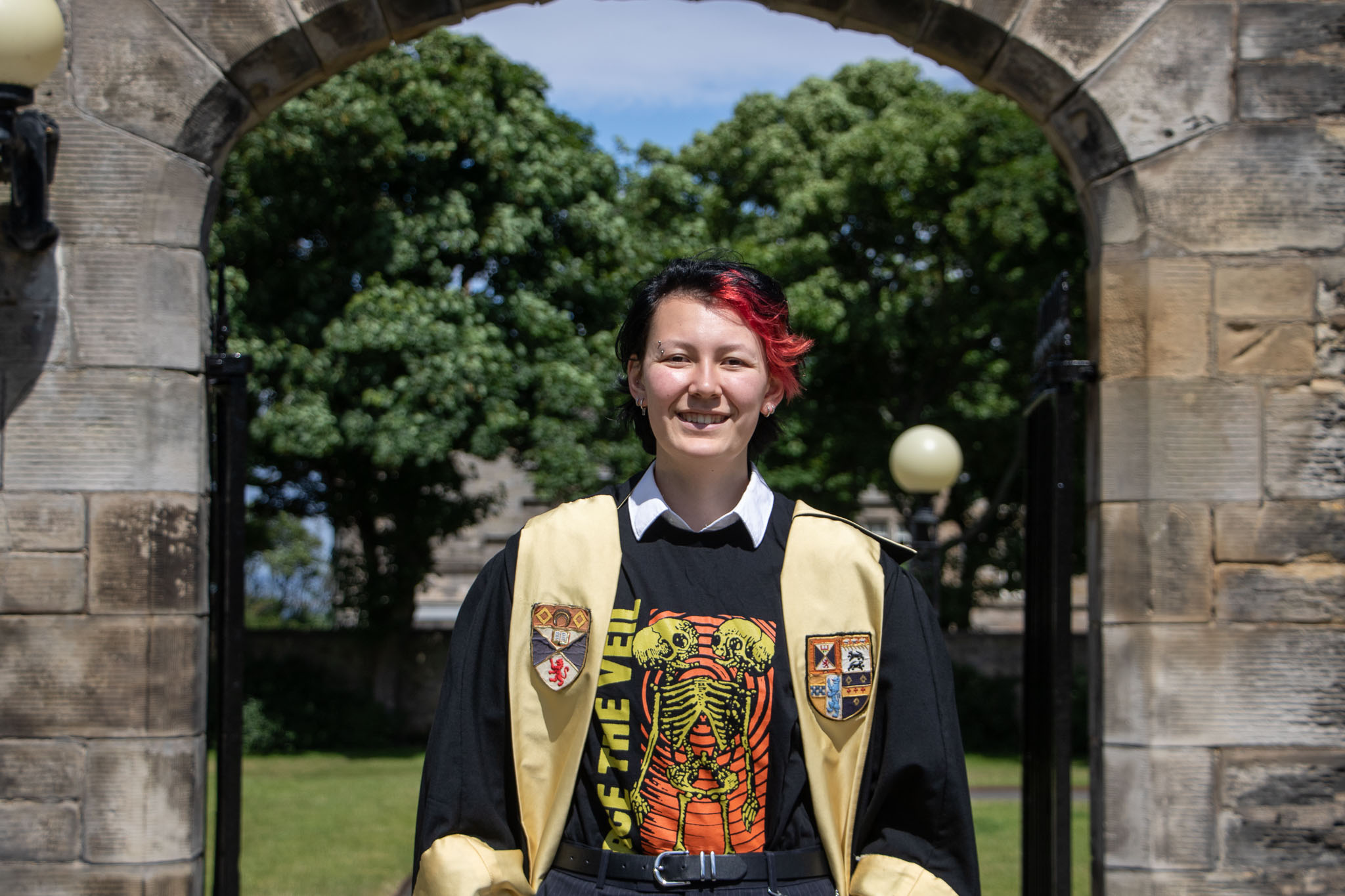 Milo smiles in his black gown. The gown is faced gold with the Association and University crests emblazoned.