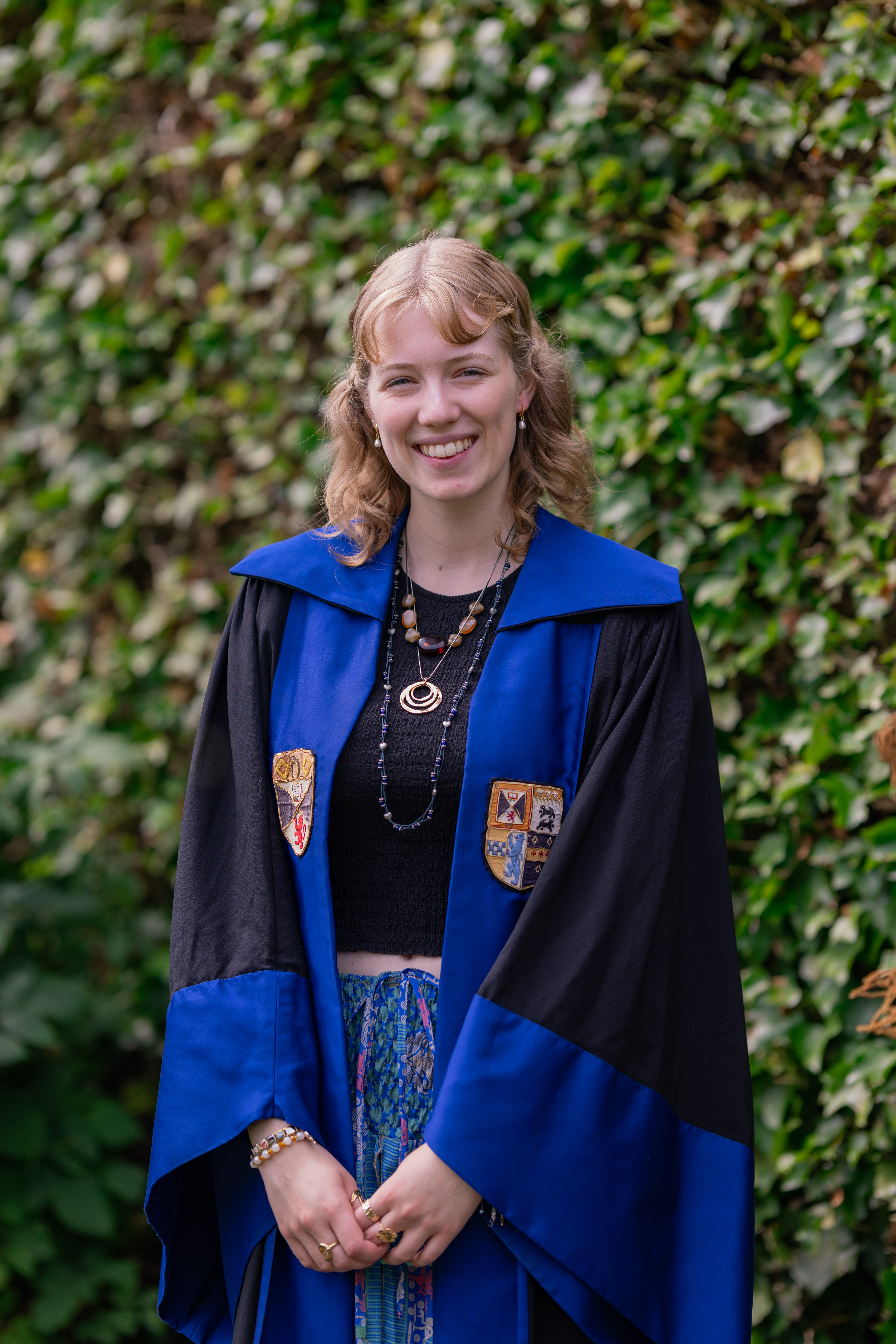 Emily smiles in the President of Education gown. The gown is faced in blue with the Association and University crests emblazoned.