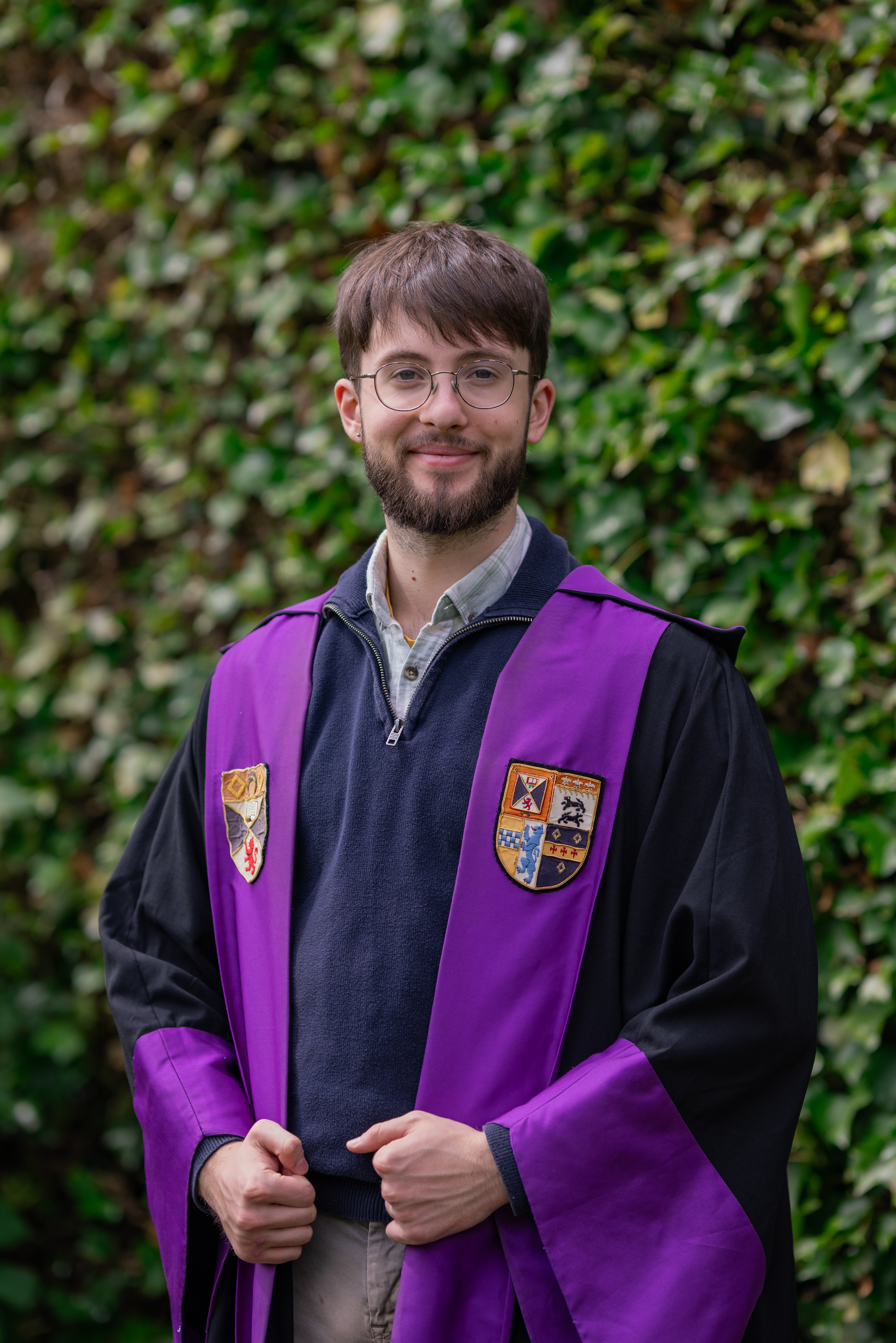 RoMo smiles in the President of Student Opportunities gown. The gown is faced purple with the Association and University crests emblazoned.