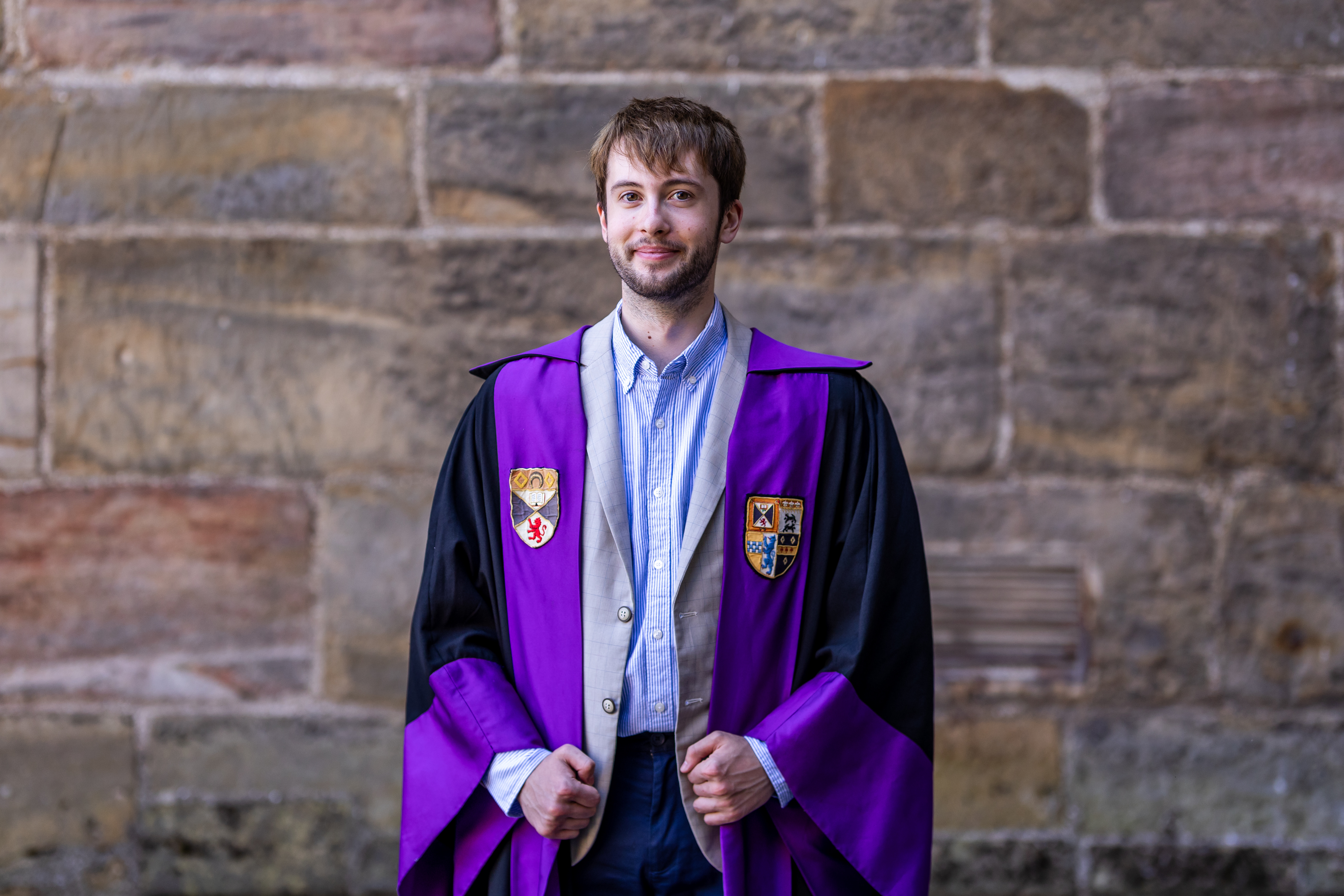 RoMo smiles in the President of Student Opportunities gown. The gown is faced purple with the Association and University crests emblazoned.