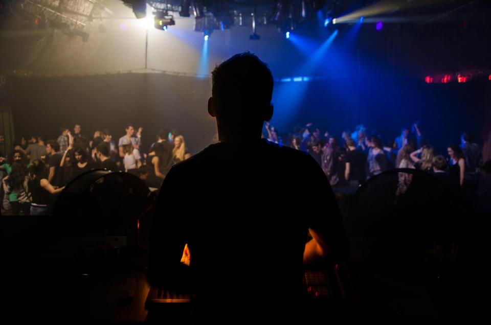 The silhouette of a DJ looks over a dancing crowd.