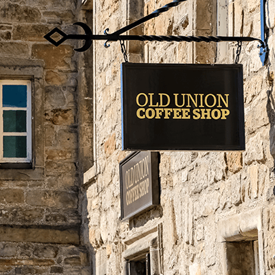 The Old Union Coffee Shop sign hangs on a tradition stone brick wall.
